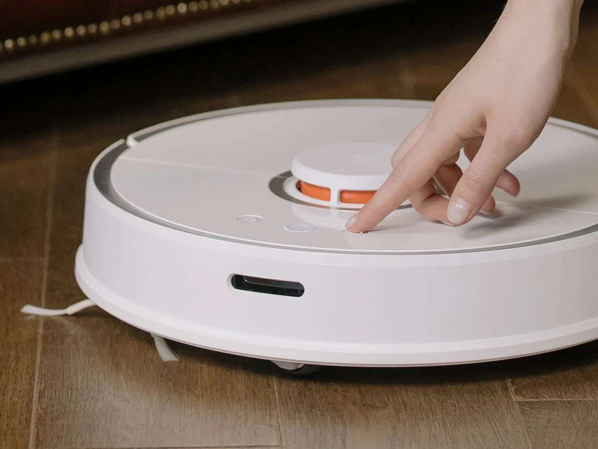 Primer plano de una mano presionando el botón de una aspiradora robot
