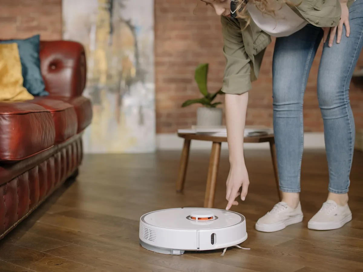 Mujer revisando una aspiradora robot en el living de su casa