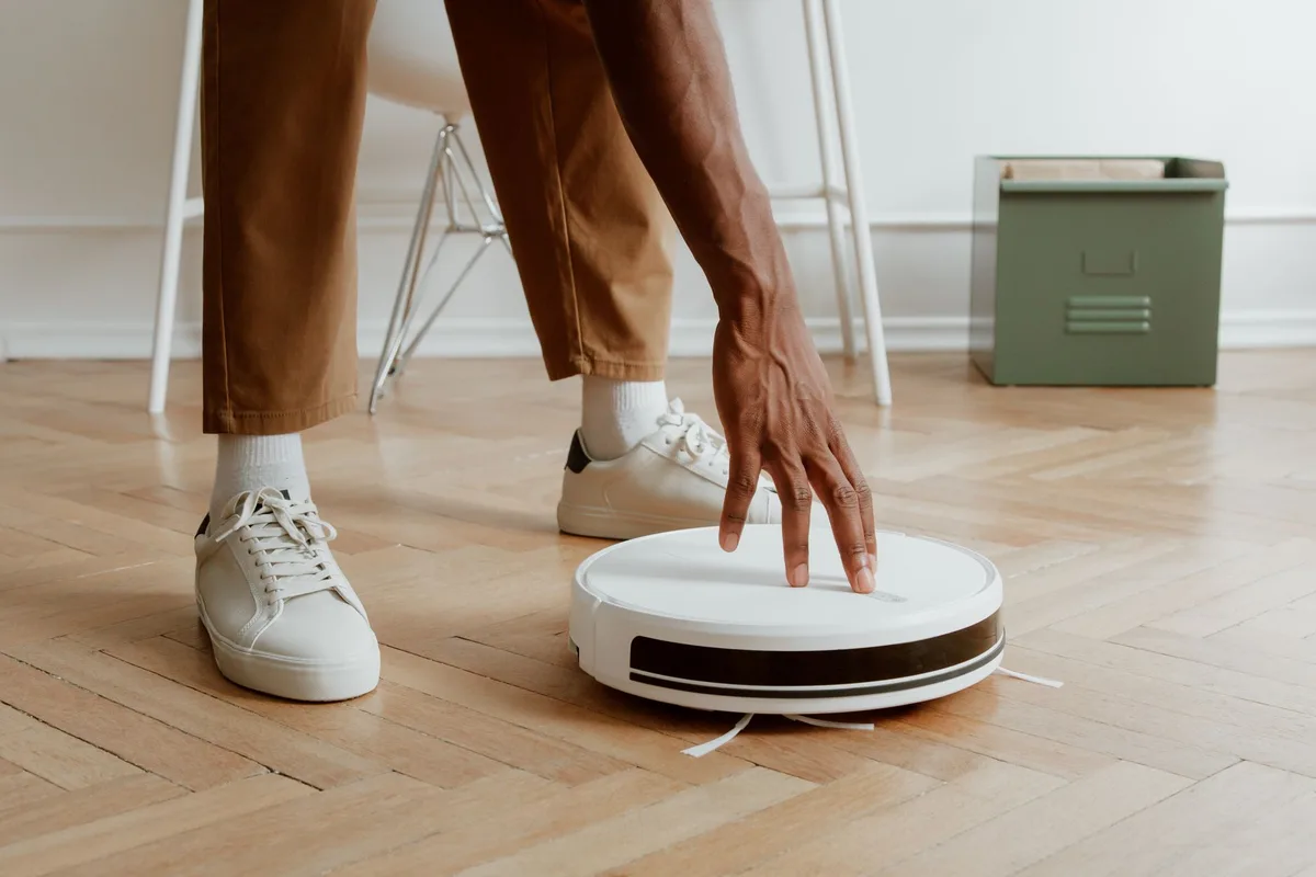 Mano ajustando los controles de una aspiradora robot sobre piso de madera